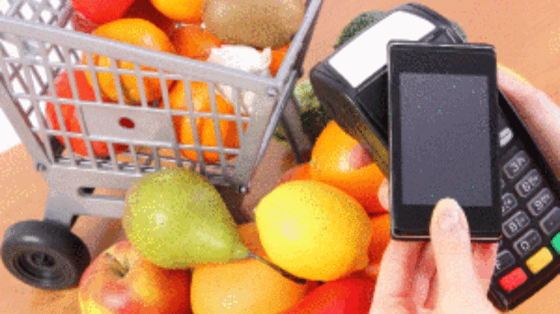 Picture of person buying fruits using phone and NFC wireless pay terminal.